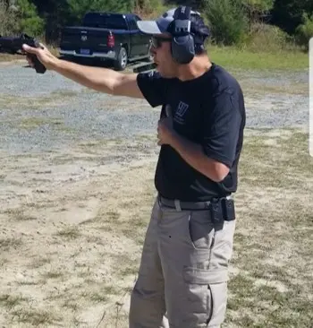 A man in black shirt holding a gun on top of grass.